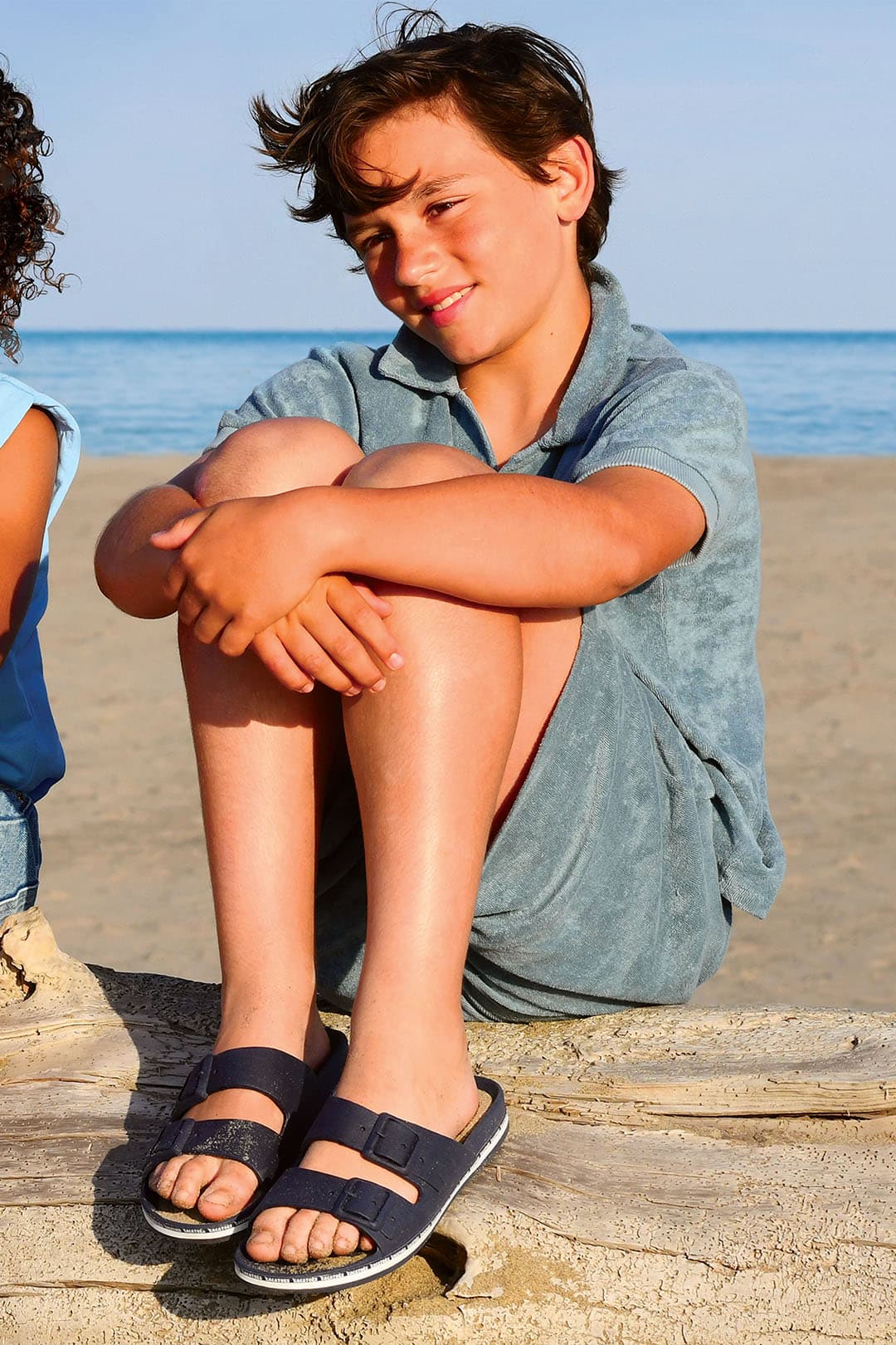 Enfant assis à la plage portant des sandales bleu foncé